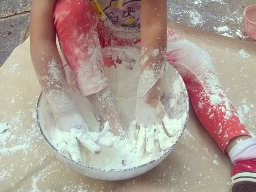 una niña sentada en una actividad de lluvia de luna, explorando texturas, en este caso tenemos un bowl con maicena, la niña explora las texturas con las manos y con uno de sus pies.